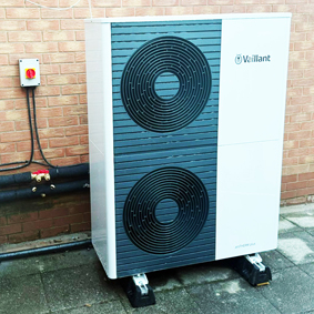 A two fan Mitsubishi heat pump situated next to a wall outside a house.