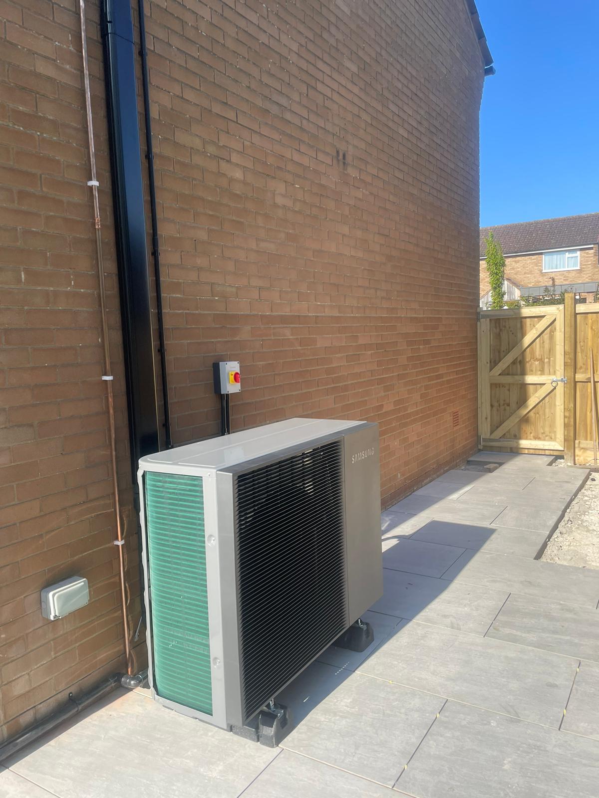 An air source heat pump fan situated next to a wall on a semi detached home. 