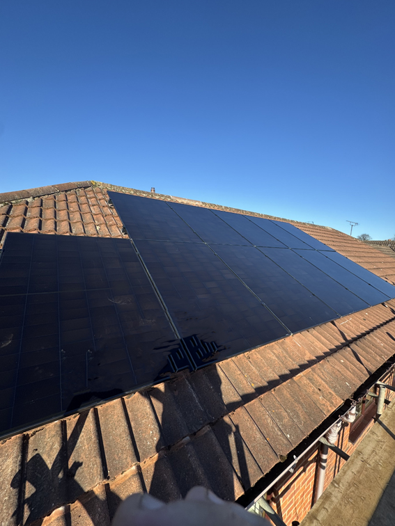Black on black solar panels situated on a pitched roof on a sunny day. 