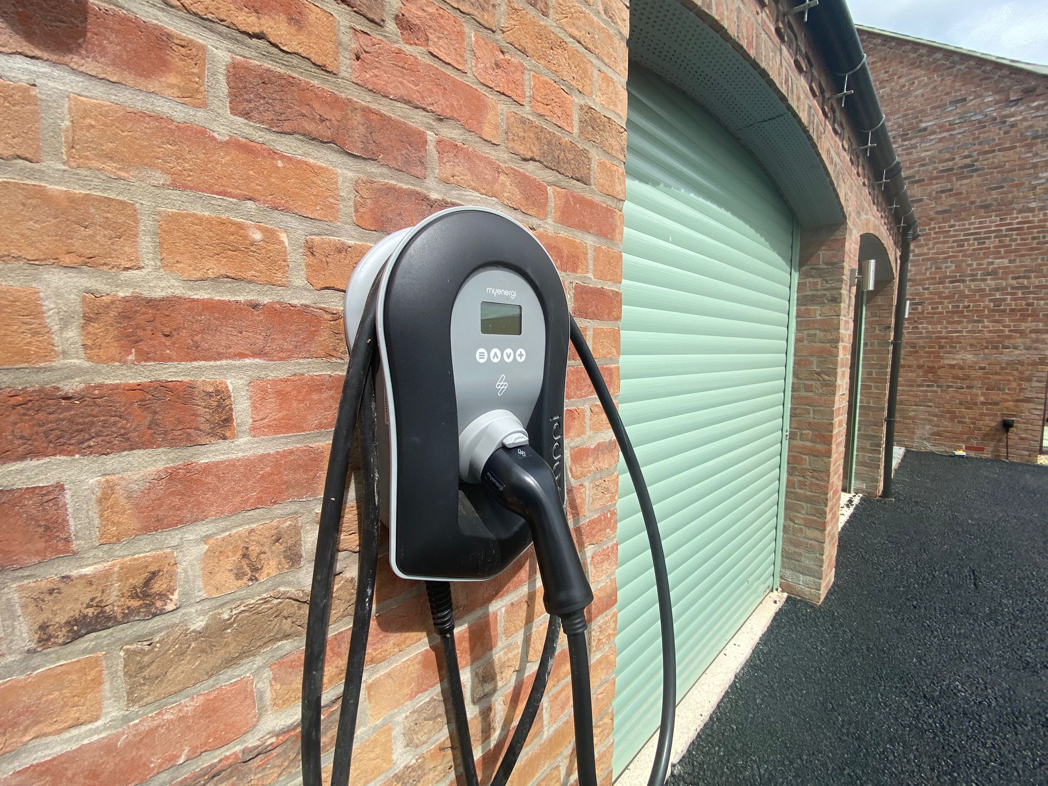 A Zappi Electric Car Charger mounted on the wall of a double garage with green doors