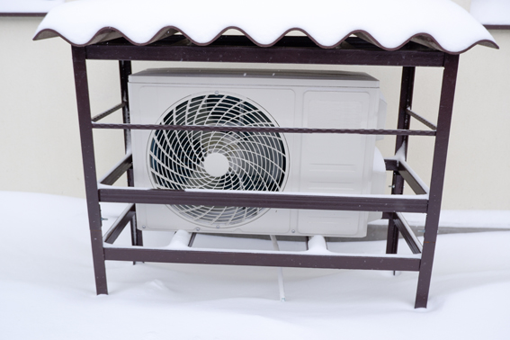The fan unit of an air source heat pump fitted under a shelter - the shelter is covered in snow.