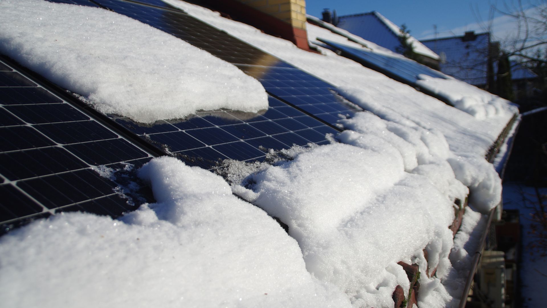Solar panels on a roof with snow on top of them.